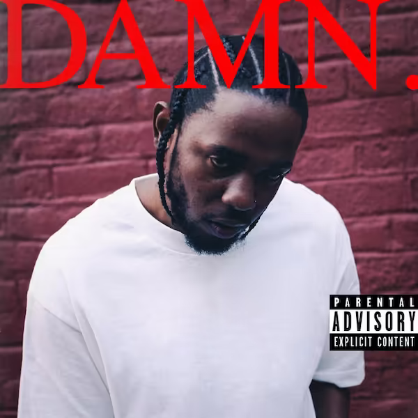 Lamar dressed in a off-white shirt, behind is red brick wall.