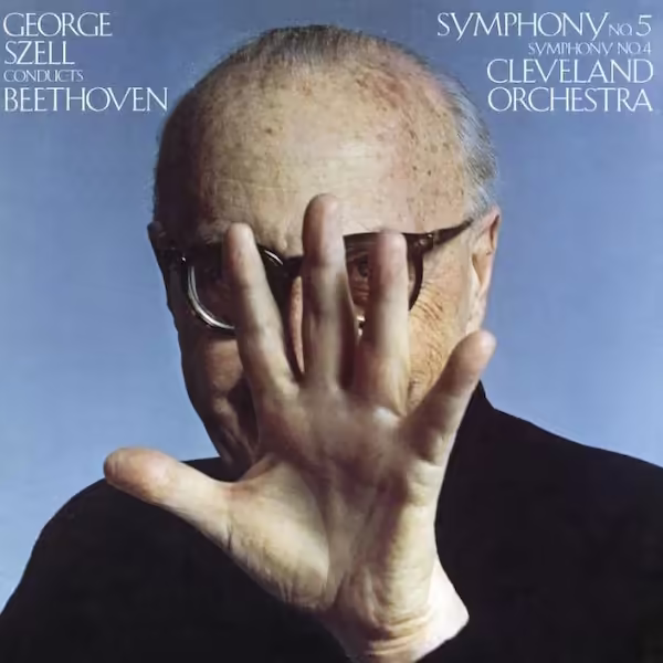 George Szell holds his hand toward the foreground blocking the view of his face. The background is a light blue.