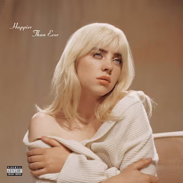 Eilish with blonde hair and a white off-the-shoulder jacket, hugging herself, while tears fall from her right eye. Behind her is a backdrop colored brown.