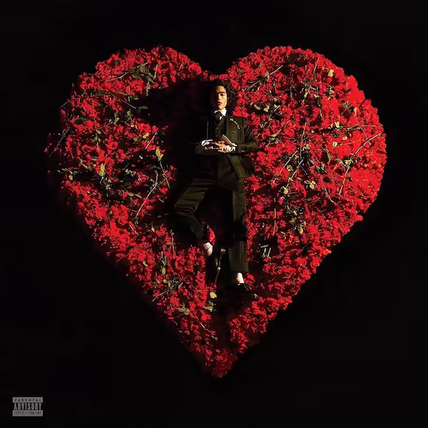 Gray lies in a heart-shaped pile of red roses on a black floor.